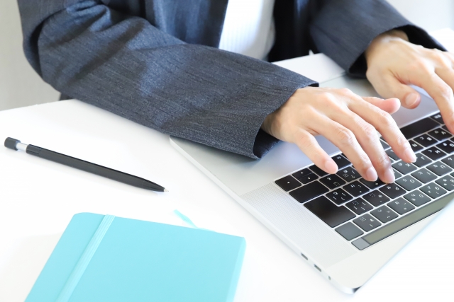 デスクでパソコンをタイピングするジャケットを着た人