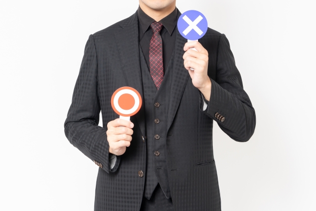 バツの札を上げるスーツ姿の男性